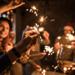 Close up of unrecognizable man holding sparkler during a party with group of his friends.